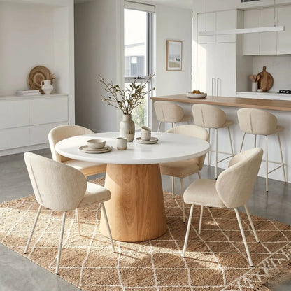 Round microcement dining table with natural oak base, linen dining chairs in an modern open plan kitchen dining apartment by sun republic