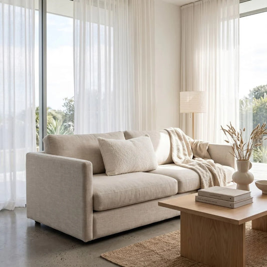 Beige sofa in a modern living room with large windows and a wooden coffee table.