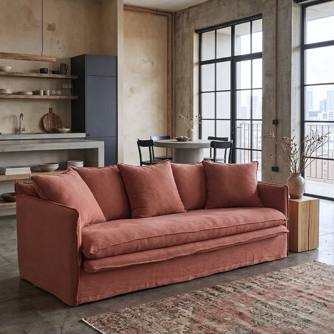 linen desert rose colour sofa, in a modern living room with large windows and a kitchen area.