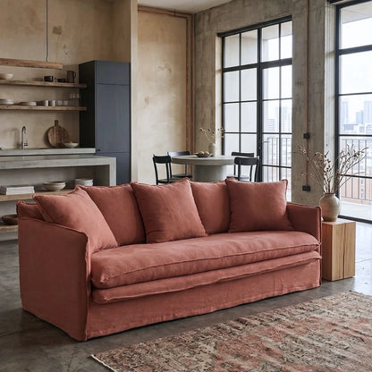 linen desert rose colour sofa, in a modern living room with large windows and a kitchen area.