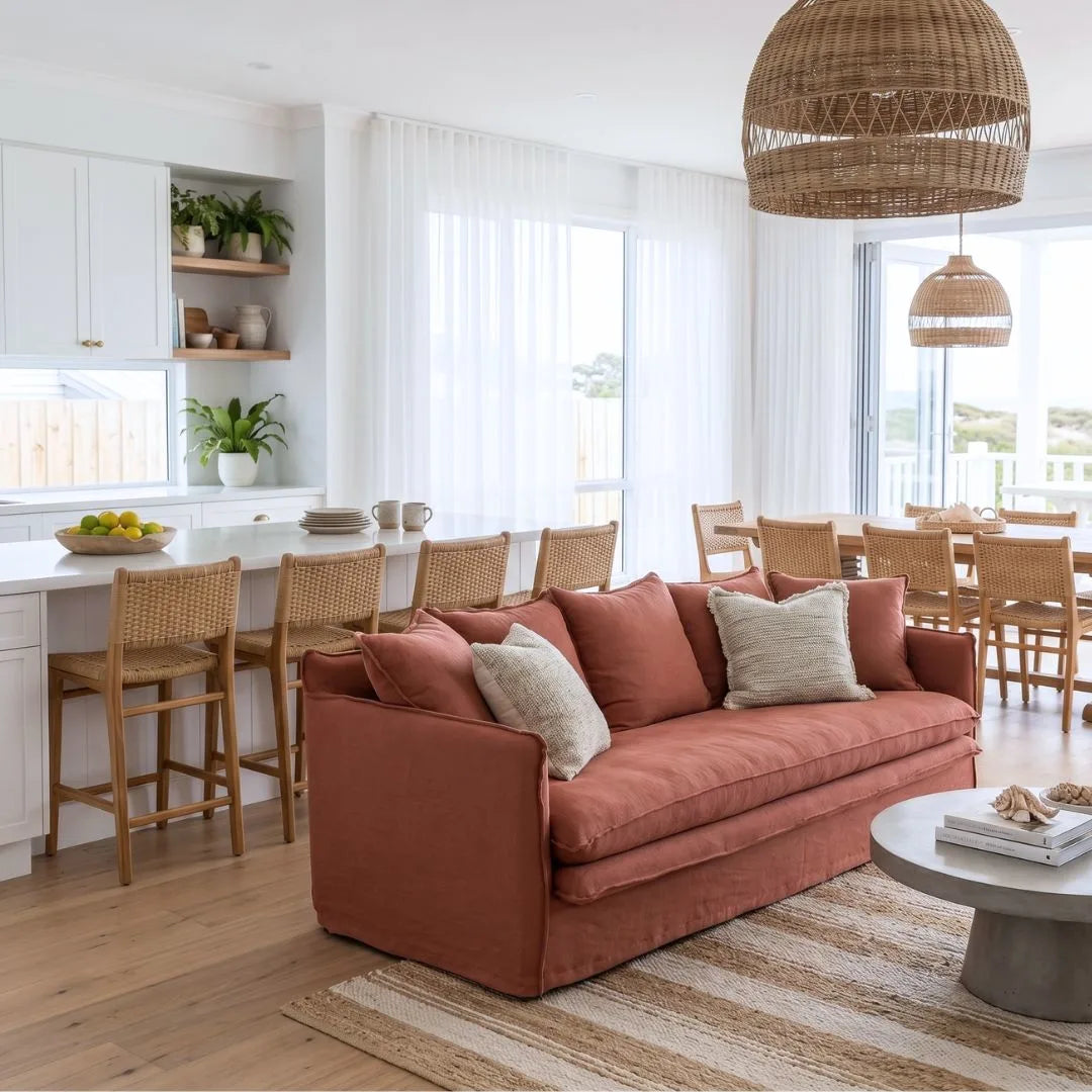 Living room with a linen desert rose colour sofa, wooden chairs, and a dining area in the background.