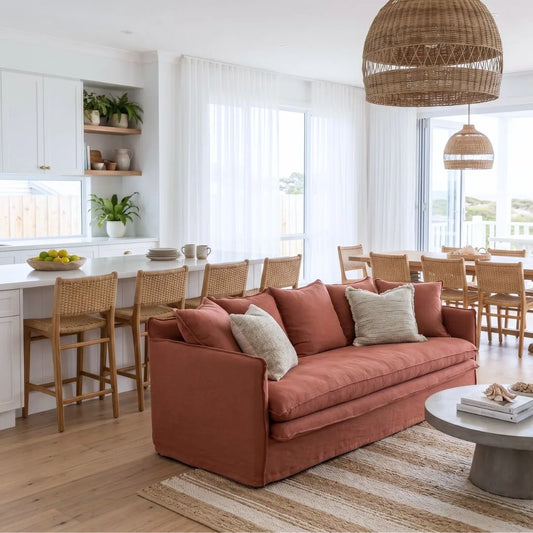 Living room with a linen desert rose colour sofa, wooden chairs, and a dining area in the background.