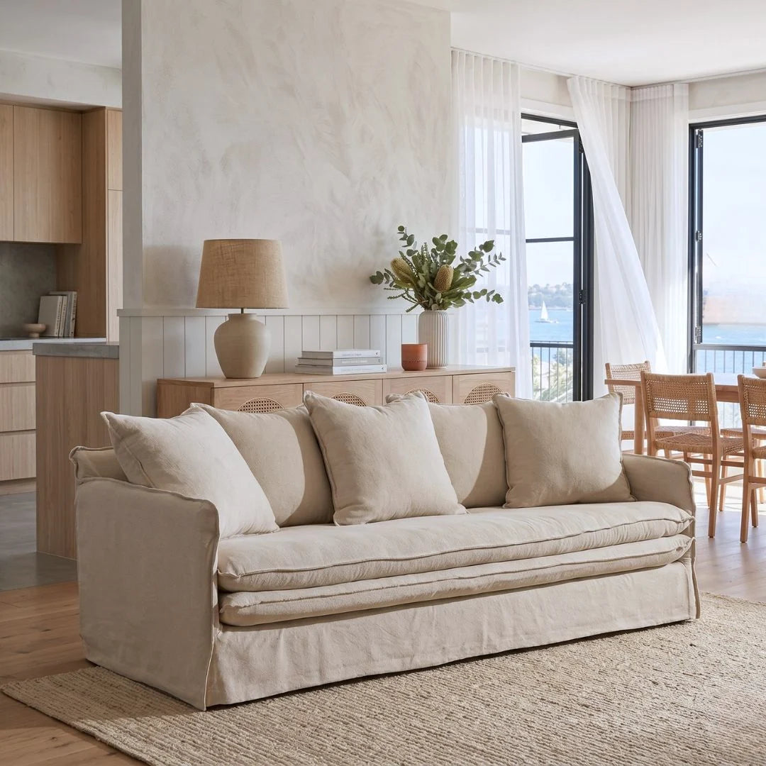 Beige sofa in a living room with a lamp, plant, and window view.
