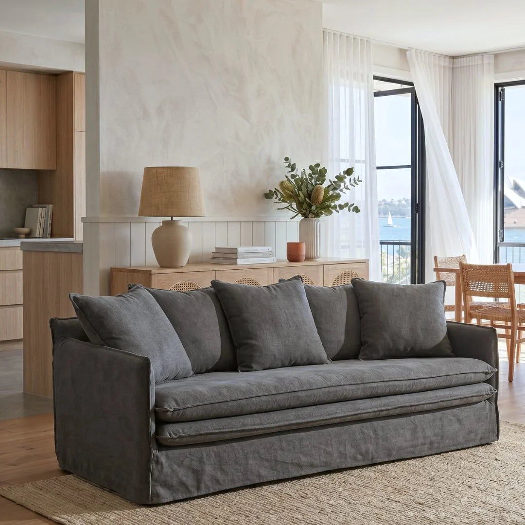 Gray sofa in a living room with a lamp and plants on a wooden sideboard.