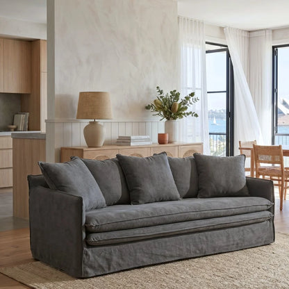 Gray sofa in a living room with a lamp and plants on a wooden sideboard.