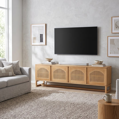 A light natural wood TV stand with woven cane panel doors, styled in a modern living room under a wall-mounted flat-screen TV.