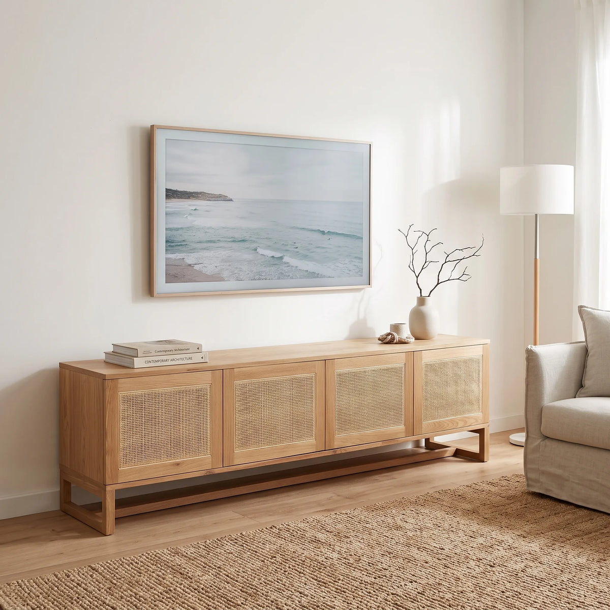 A light natural wood sideboard with woven cane panel doors, styled in a bright, modern living room under a framed ocean landscape print.