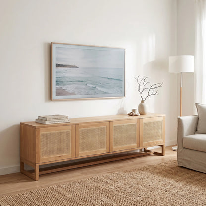 A light natural wood sideboard with woven cane panel doors, styled in a bright, modern living room under a framed ocean landscape print.