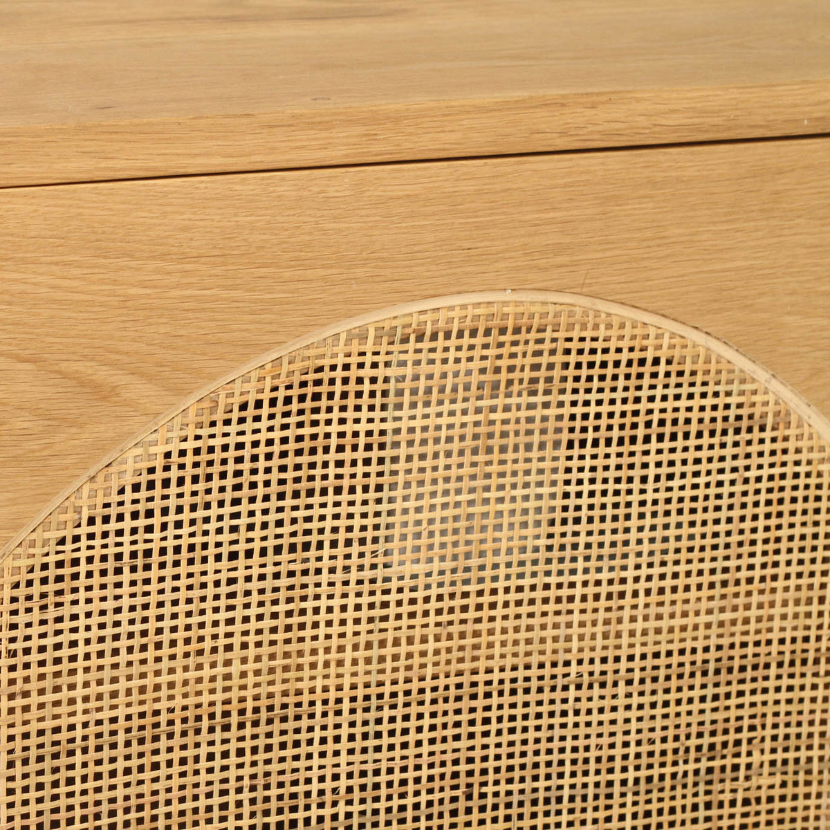 Close-up of a light natural wood cabinet corner with a woven cane or rattan panel on the front.