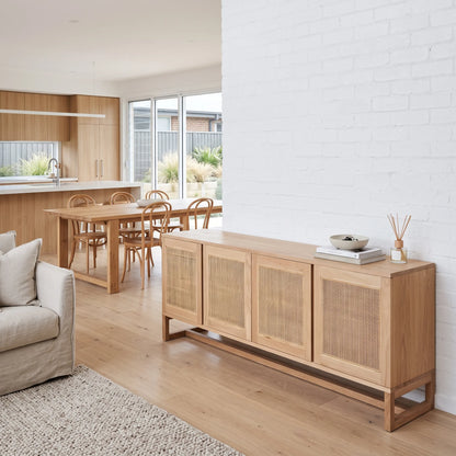 A light natural wood sideboard with woven cane doors, styled in a bright, modern open-plan living room next to a white brick wall.