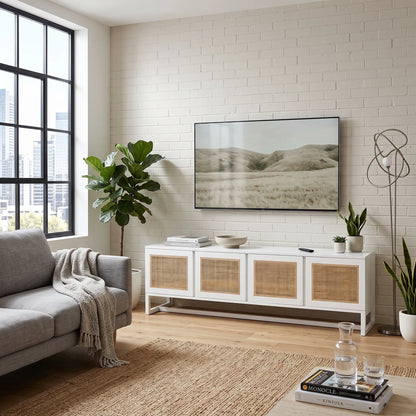A modern living room scene featuring a white media console with woven cane doors, styled with a TV, books, and plants against a white brick wall.