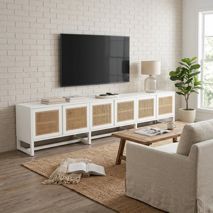 A modern white TV stand with woven rattan doors, styled in a bright living room with a brick wall, wall-mounted TV, coffee table, and armchair.