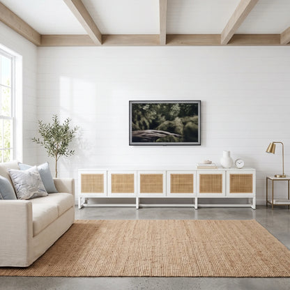 A modern living room scene featuring a white media console with woven cane doors, a mounted flat-screen TV, a beige sofa, and a large natural jute rug on a concrete floor.