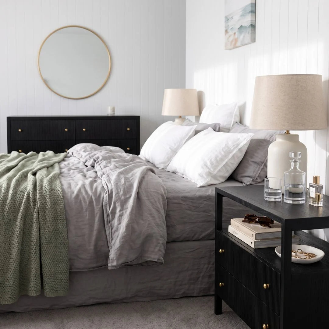 Black timber bedside table nightstand in a modern bedroom with matching black chest of drawers dresser