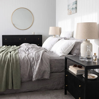 Black timber bedside table nightstand in a modern bedroom with matching black chest of drawers dresser
