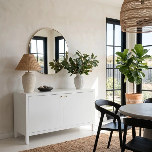 Modern interior with white sideboard, round mirror, and potted plants.