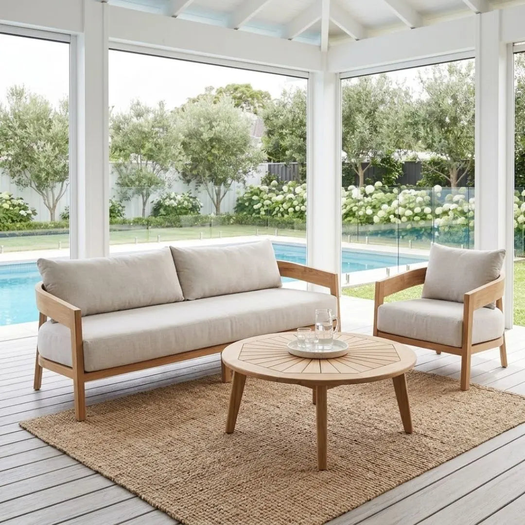 Outdoor patio set with wooden furniture and beige cushions on a deck with a pool view.