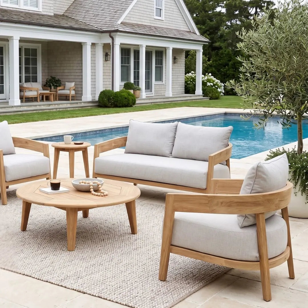 Outdoor patio set with wooden furniture and white cushions by a poolside.