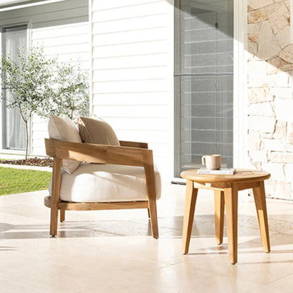 Wooden outdoor chair and table set on a patio with a stone wall and garden in the background.