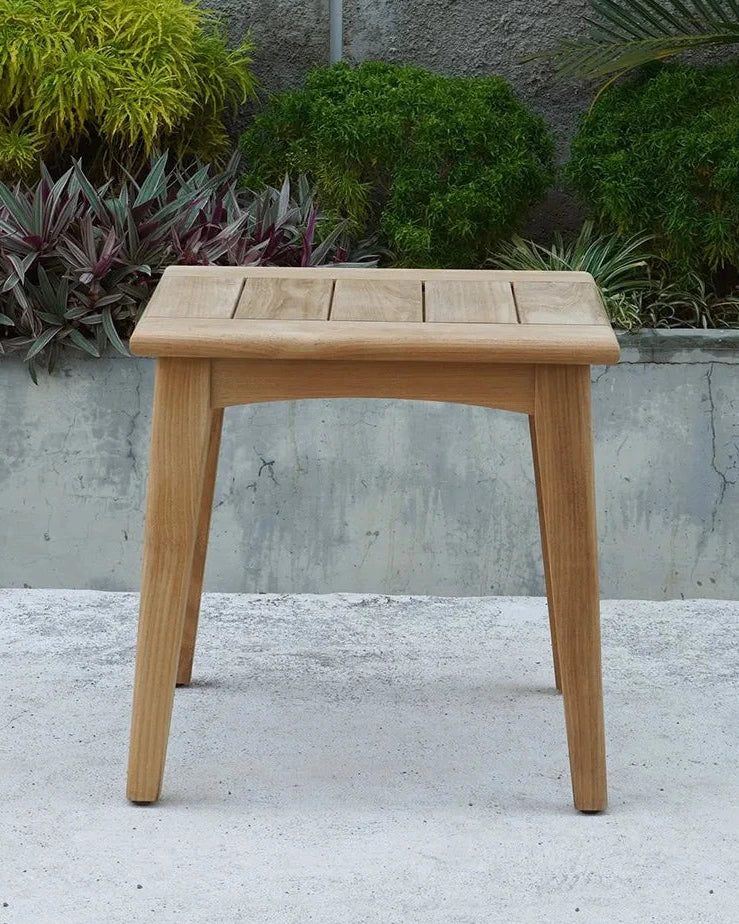 Wooden side table on a concrete surface with a gray wall and plants in the background