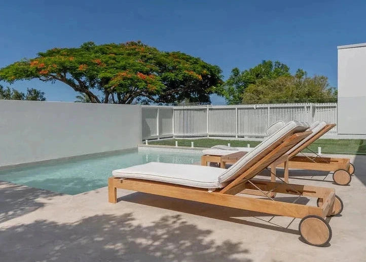 Wooden lounge chairs by a pool with trees and clear blue sky in the background