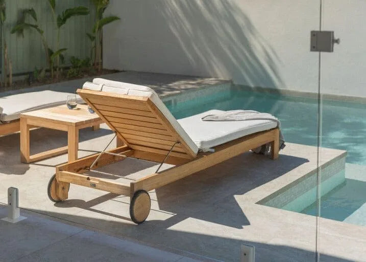 Wooden lounge chair with white cushions by a poolside