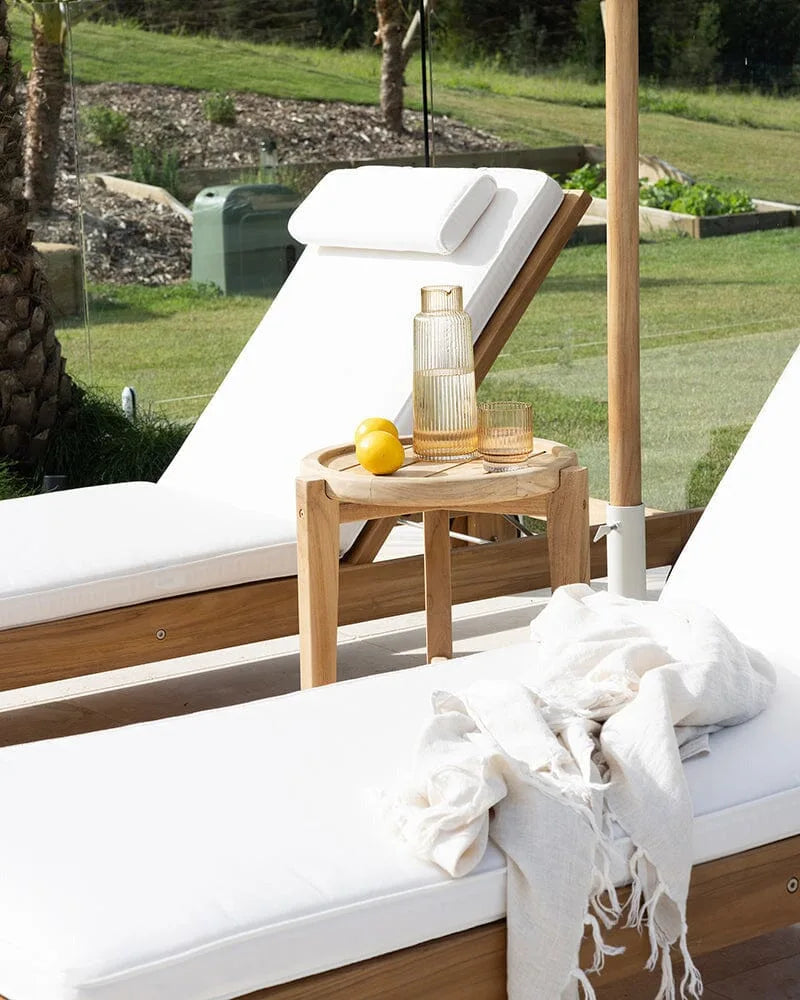 Two white lounge chairs with wooden frames and a small table with decorative items on a grassy outdoor area.