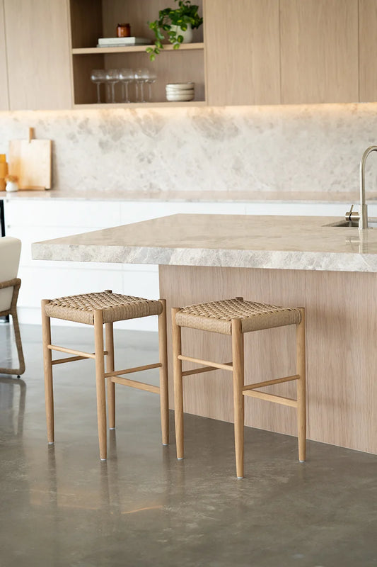 Two wooden stools with woven seats in a modern kitchen setting.