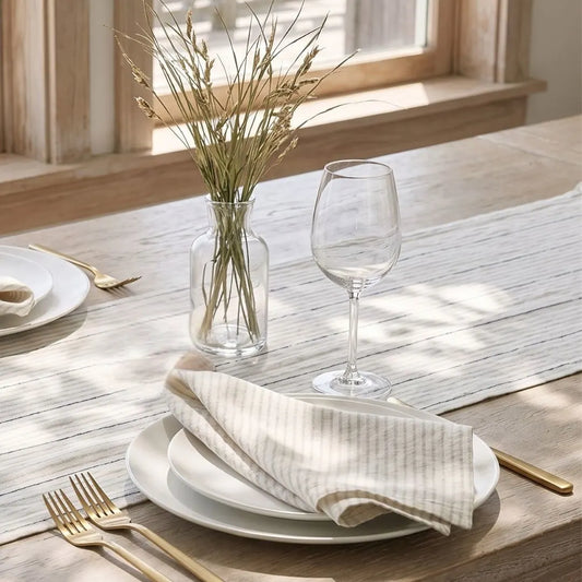 Dining table setting with plates, glasses, and a vase on a wooden surface.