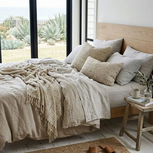 Cozy bedroom with a bed featuring beige linens and pillows, a wooden headboard, and a small table with a plant.