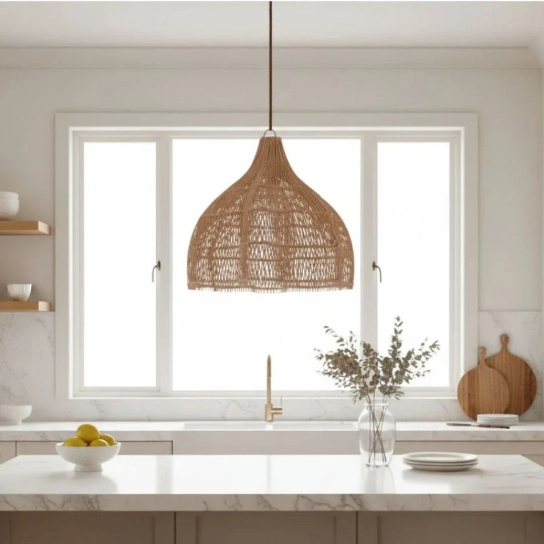 Modern kitchen with a sun republic woven rattan pendant light, marble island, and white cabinets.