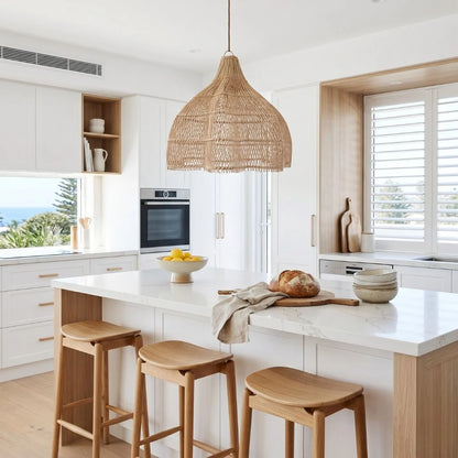 Modern kitchen with white countertops, wooden stools, and a lotus rattan pendant light.