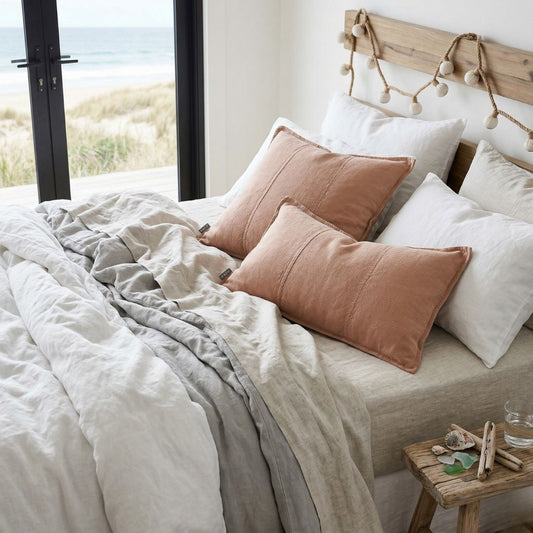 Bed with beige and brown pillows and a wooden headboard in a room with a view of the ocean.