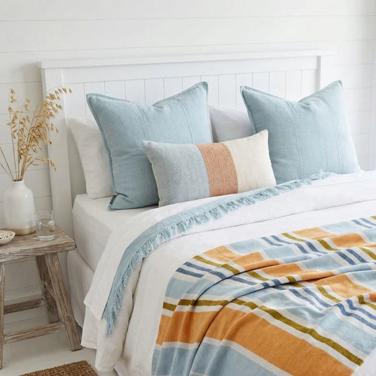Bed with light blue pillows and a colorful striped blanket in a bright bedroom.