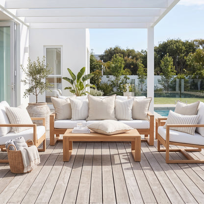 Outdoor patio furniture set with light wood frames, white cushions, and striped pillows arranged on a covered deck beside a pool.
