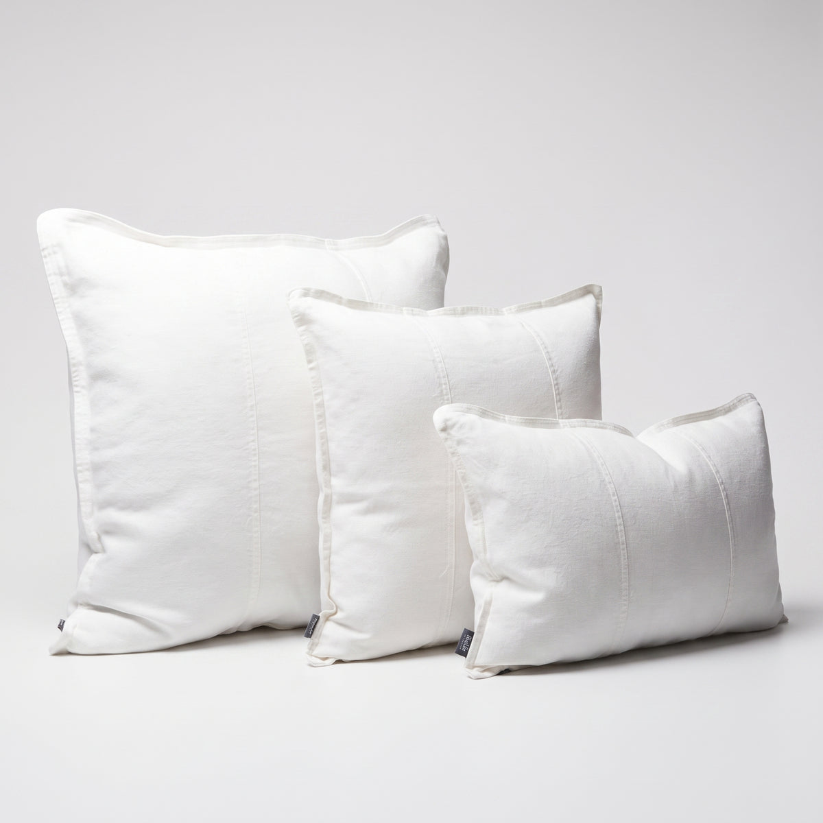 Three white textured throw pillows in different sizes arranged on a light gray studio background.