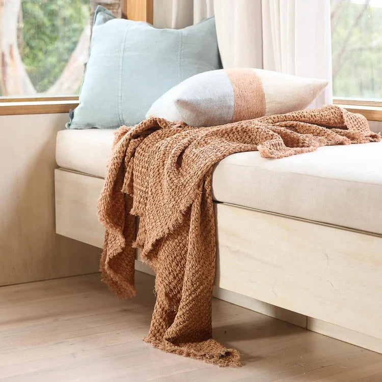 Cozy living room with a beige sofa, brown blanket, and colorful pillows.