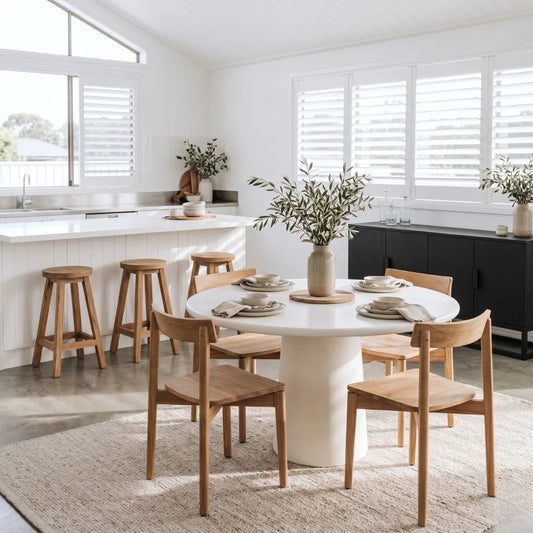 Dining area with a white round table and wooden chairs in a bright kitchen.