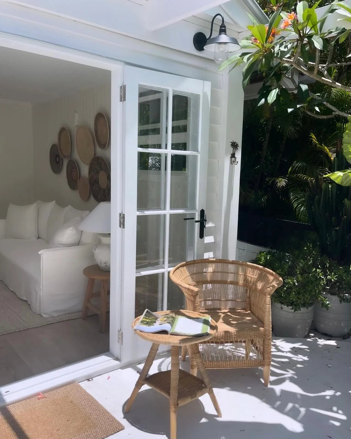 Outdoor patio area with wicker chair, table, and white sofa inside a house.