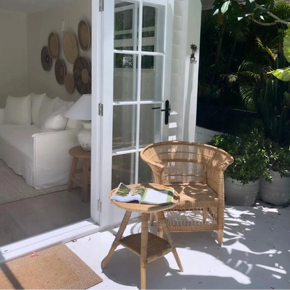 Outdoor patio area with wicker chair, table, and white sofa inside a house.