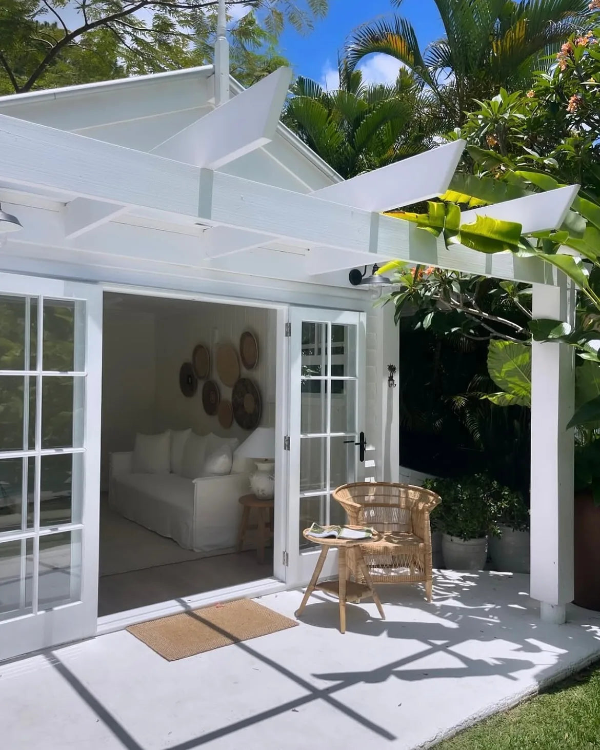 White outdoor pavilion with a couch, chairs, and decorative items in a garden setting.