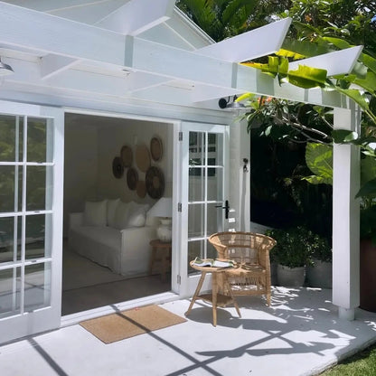 White outdoor pavilion with a couch, chairs, and decorative items in a garden setting.