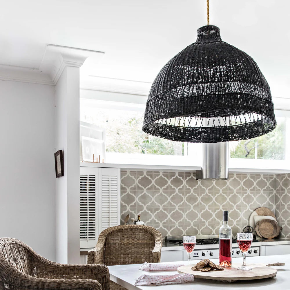 Black woven pendant light hanging in a kitchen with wicker chairs and a table.