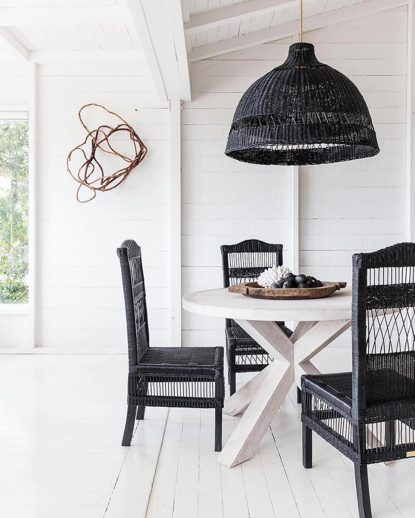 Dining area with black wicker chairs and a round table under a black woven pendant light.