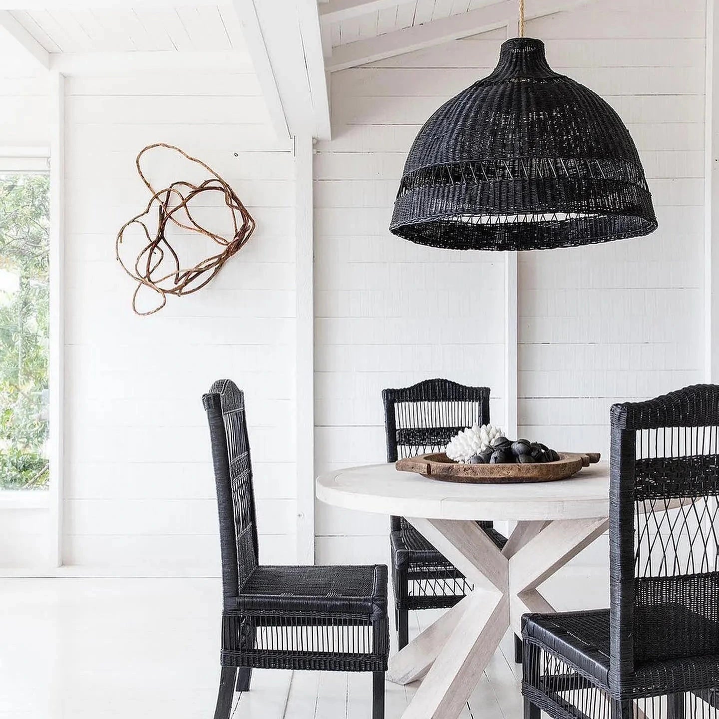 Dining area with black wicker chairs and a round table under a black woven pendant light.