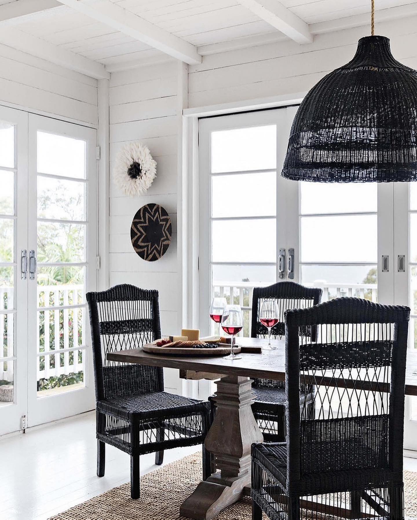 Dining area with black wicker chairs and a round table, featuring sun republic black woven decorative pendant light.