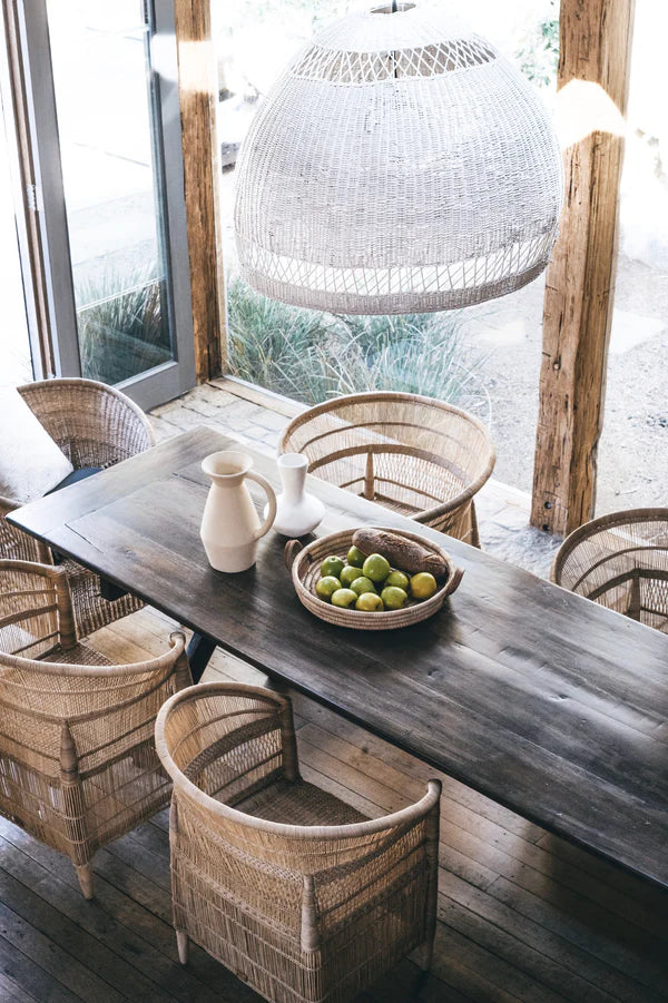Dining area with wooden table and wicker chairs, featuring a bowl of apples.