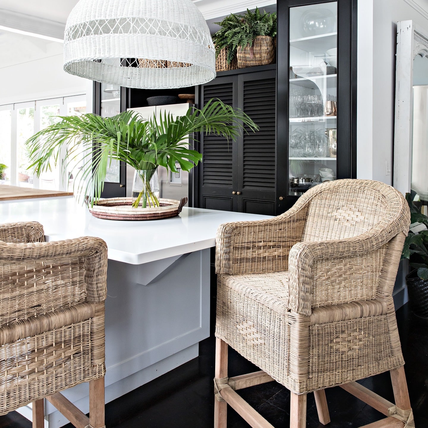 Wicker bar stools in a modern kitchen setting with white countertops and black cabinets.