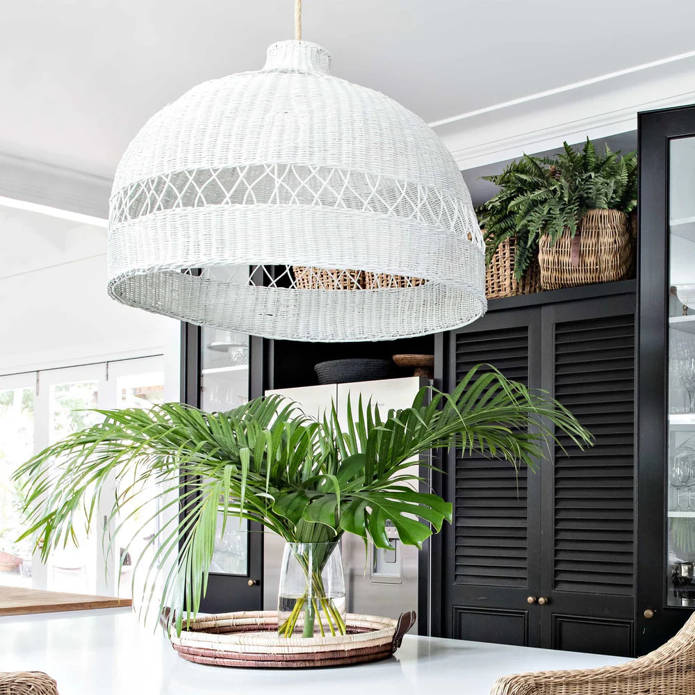 White woven pendant light fixture in a room with plants and black cabinets.