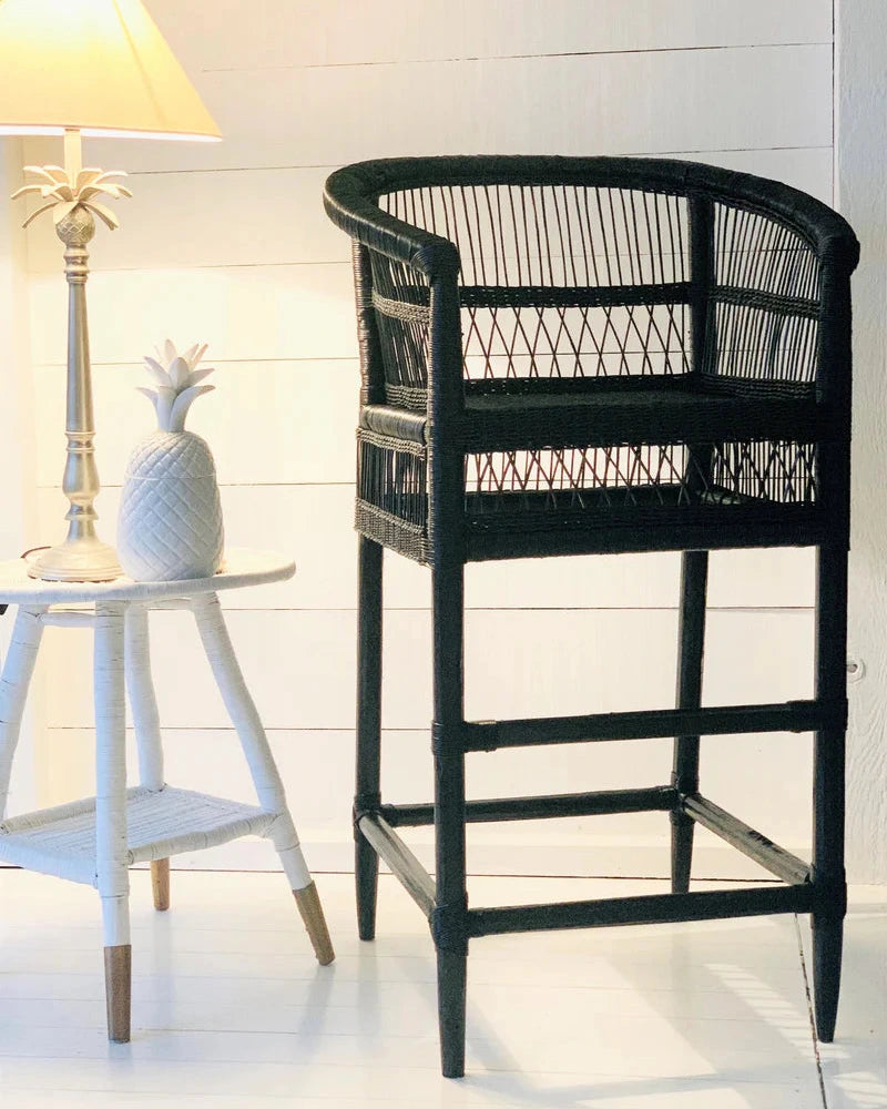 Black wicker bar stool in a room with a white wall and small table.